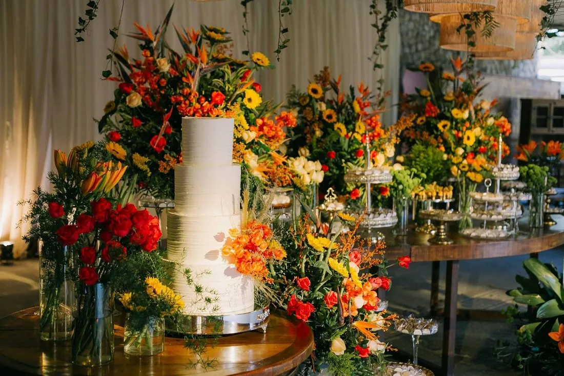 Bolo de casamento cercado de arranjos florais em tons quentes